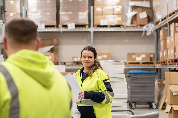 Dispatch staff member in a high visibility jacket preparing packed funeral stationery orders in a warehouse